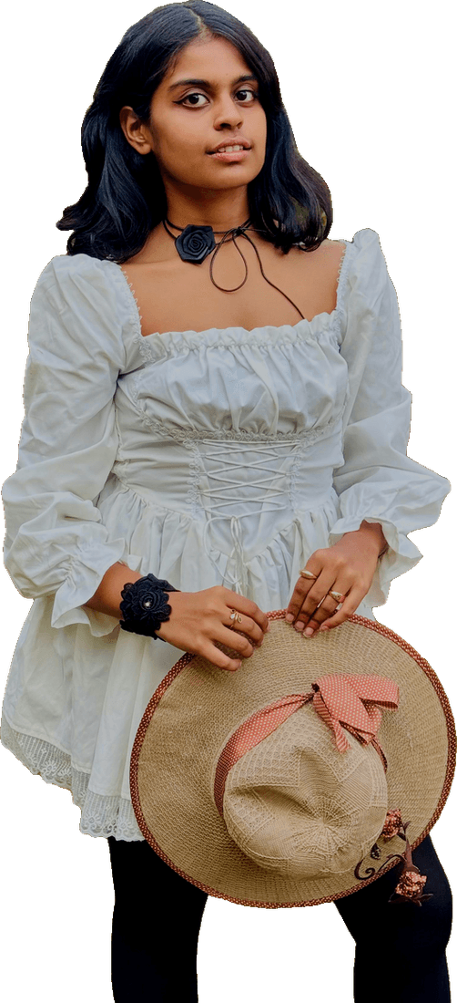Riya in a white ruffled dress holding a straw hat